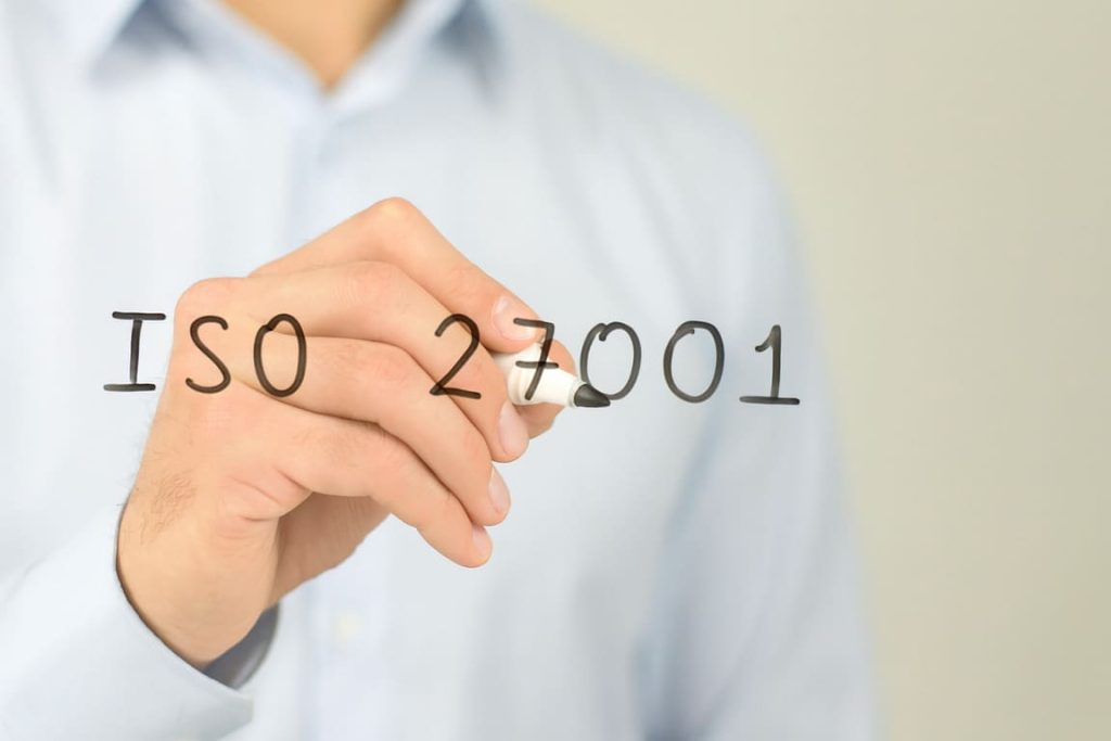 Człowiek pisze markerem „ISO 27001” na przezroczystej tablicy.